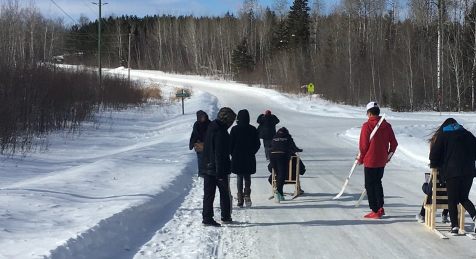 A group of students riding kicksleds down a snow covered road in Big Grass River First Nation